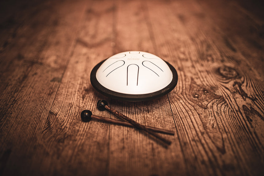 Weiße NINO980WH Mini Steel Tongue Drum mit zwei Schlägeln auf einem Holztisch
